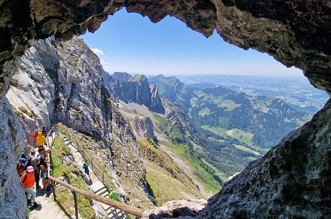 Green valleys and ridges framed by a window in a rock face, walkers on the path