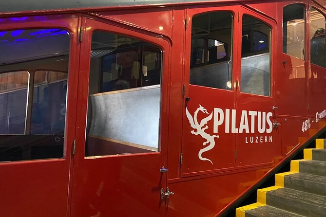 The side of a red cogwheel railcar with a white dragon emblem, at a stepped platform