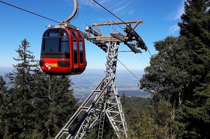 A red gondola cabin passing a pylon above pine forest, a lake far below