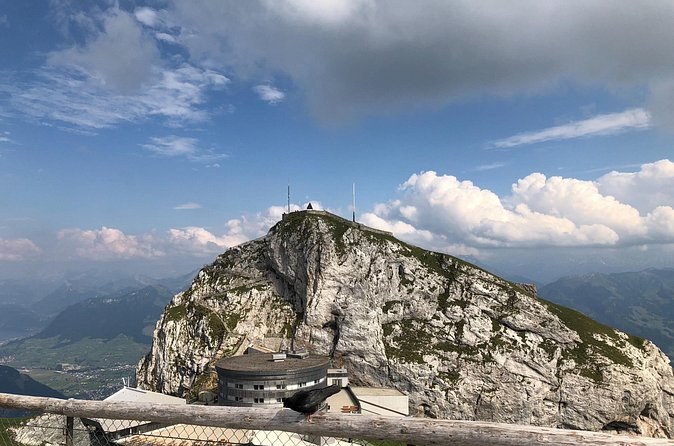 A pale limestone peak with a building on its top, under white summer cloud