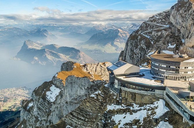 Summit buildings on a rocky crest, with a sea of cloud and far peaks beyond